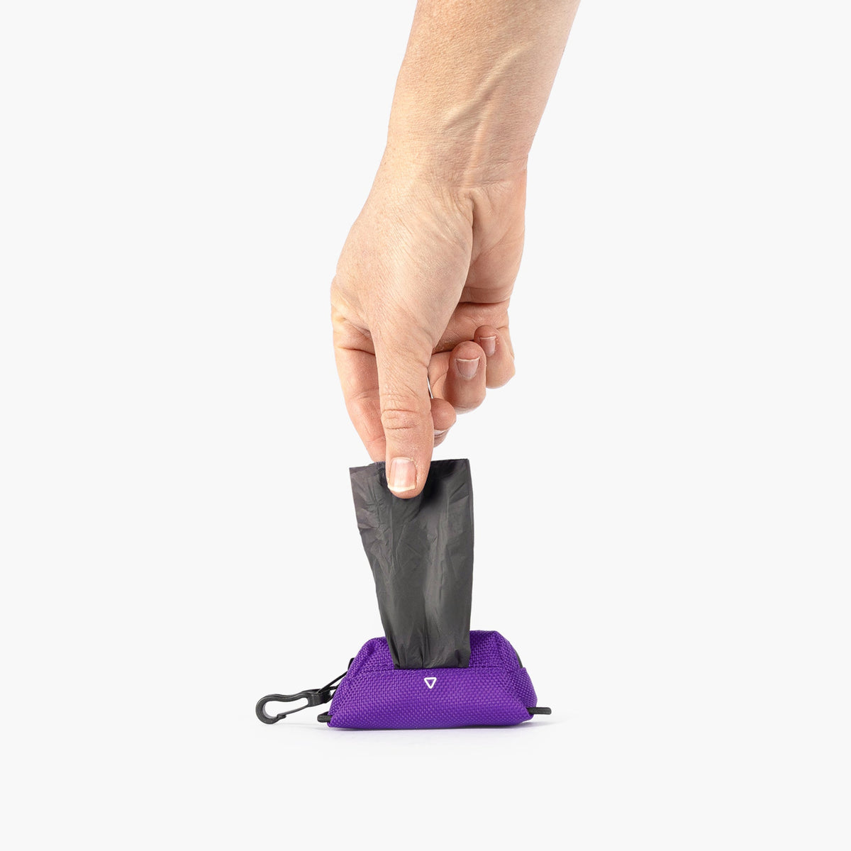Hand holding a black poop bag over a purple Essential Dog Poop Bag Holder on a white background